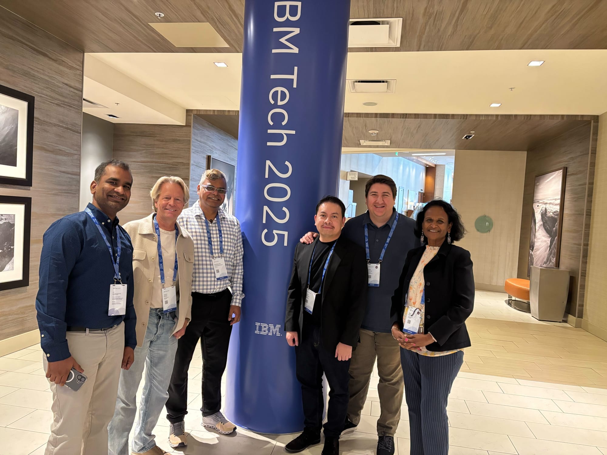 Six IBM Tech attendees posing near event signage
