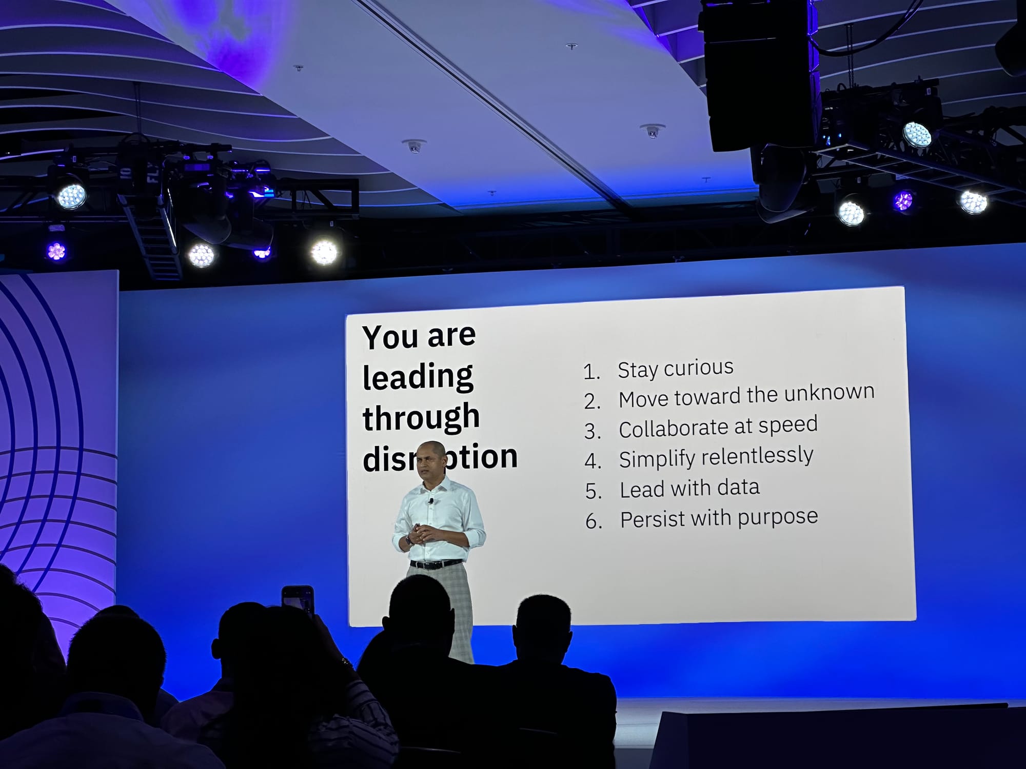 Dinesh presenting in front of a slide showing the six leadership behaviors